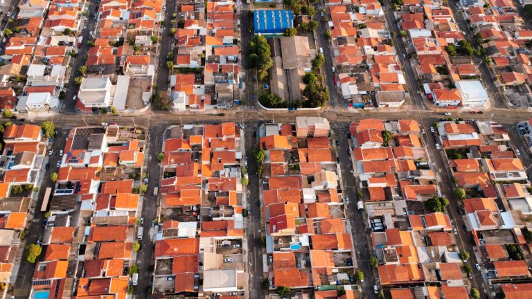Vista aérea de um bairro urbano com casas de telhados vermelhos e áreas verdes ao redor.