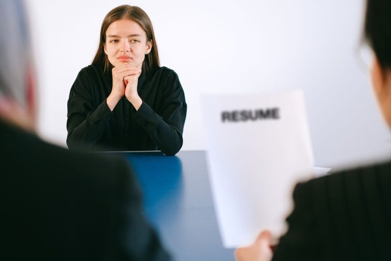 Candidata participa de entrevista de emprego diante de dois recrutadores, com o currículo em mãos.